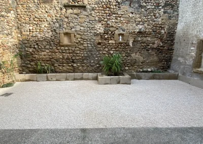 Cour intérieure après travaux, gestion des eaux pluviales, sol perméable, finition en gravier calcaire, jardinière en molasse taillée sur mesure à Alixan