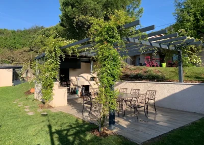 Cuisine d'été en partie fermée avec four à pain, tourne broche, évier et plan de travail, terrasse carrelée, tonnelle métallique sur mesure, couverture en rosier grimpant à Clérieux